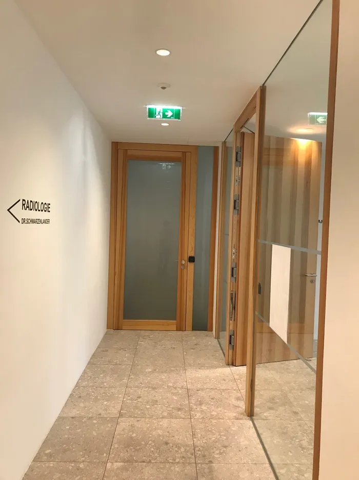 Flur mit Glastüren zur Radiologie Dr. Schwarzelauer und grünem Notausgangsschild an der Decke