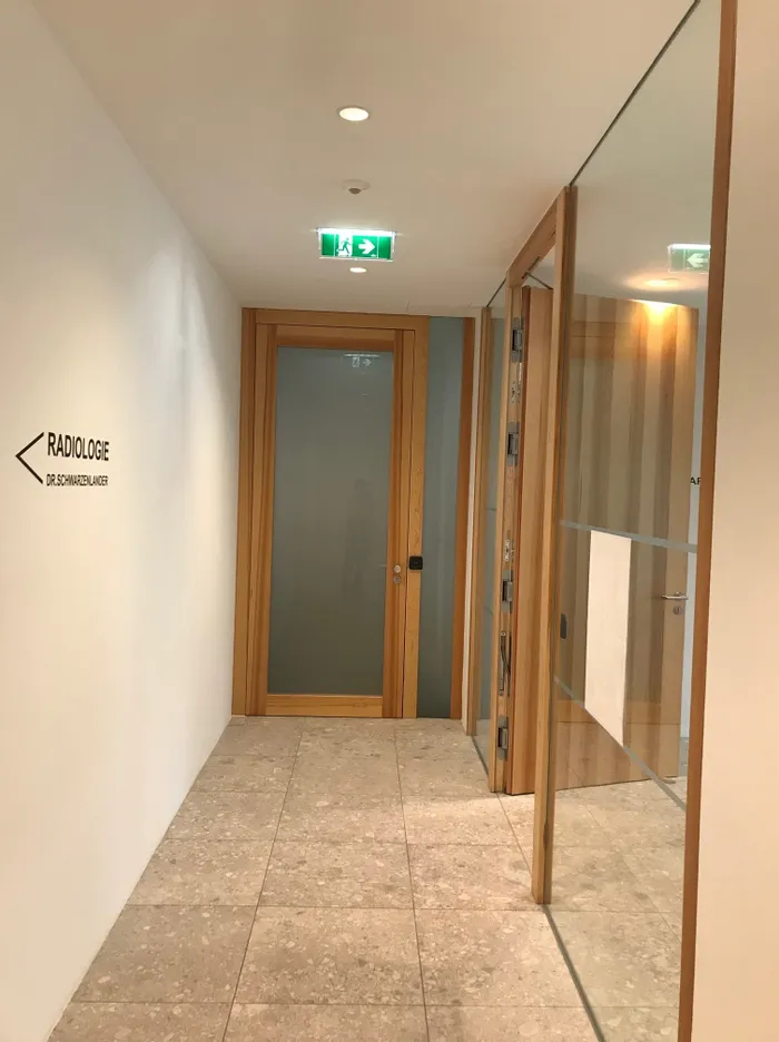 Flur mit Glastüren zur Radiologie Dr. Schwarzelauer und grünem Notausgangsschild an der Decke