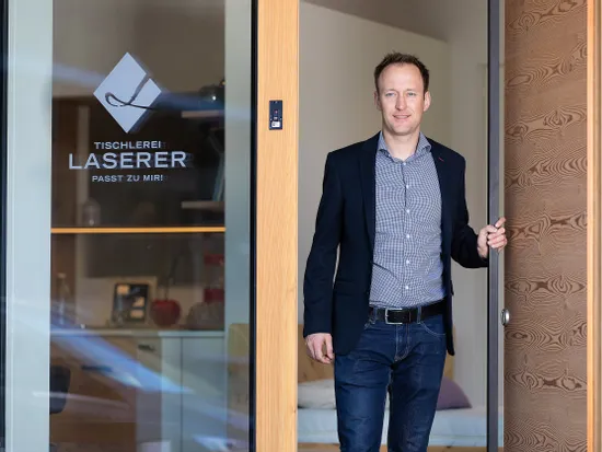 Geschäftsmann steht in geöffneter Holztür der Tischlerei Laserer