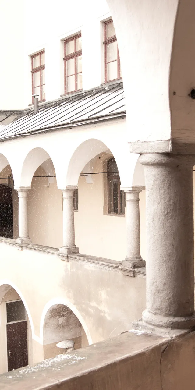 Innenhof mit Arkadengängen und Steinsäulen bei Schneefall in einem historischen Gebäude