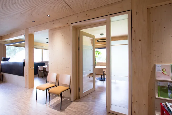 Moderne Wartezimmer mit Holzwänden und offener Tür zu Besprechungsraum mit runden Tisch und Stühlen