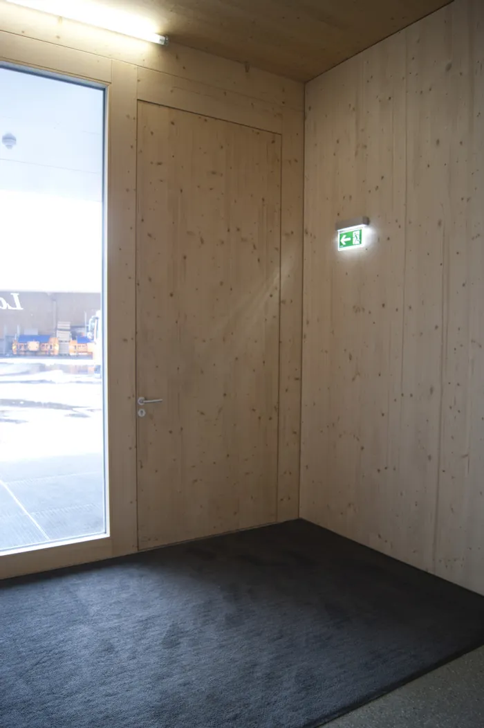 Holzverkleideter Flur mit Notausgangsschild und Tür neben großem Fenster