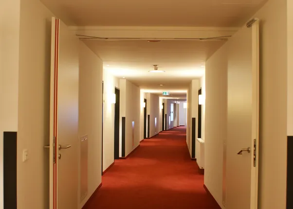 Modern hotel hallway with red carpet and white walls under warm lighting