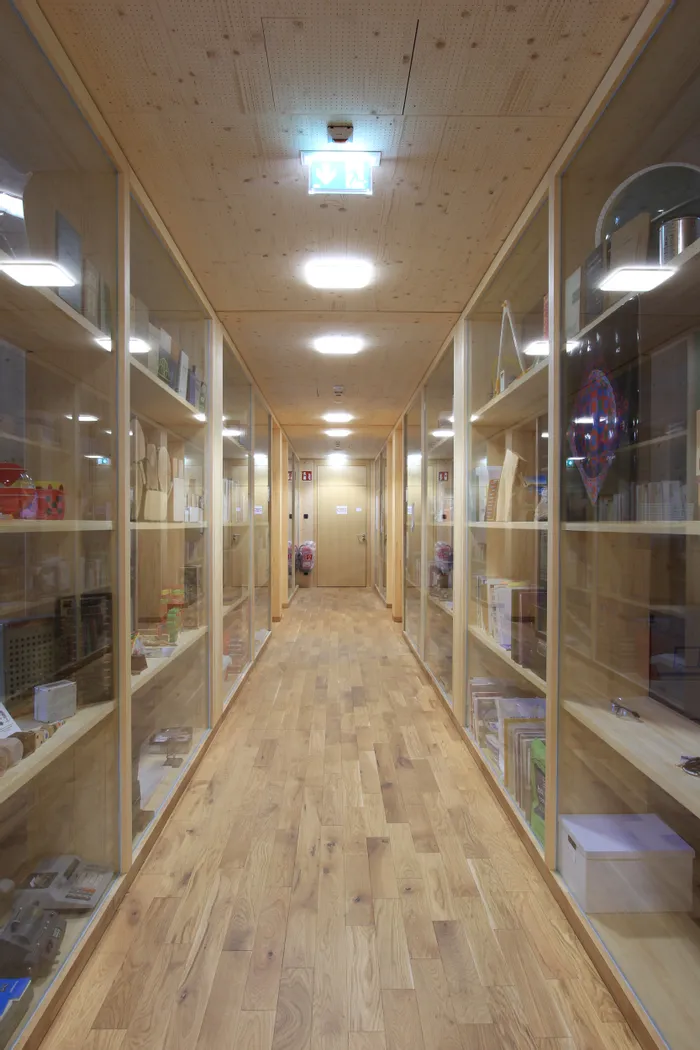 Langer Holzflur mit Glasvitrinen voller Bücher und Objekte in einem modernen Gebäude