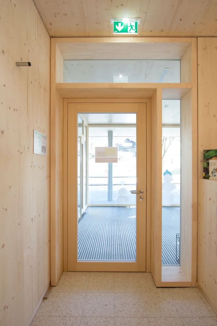 Holzverkleideter Flur mit Glastür und grünem Notausgangsschild an der Decke