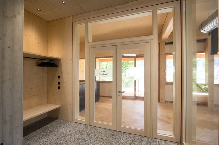 Moderner Eingangsbereich aus hellem Holz mit Glastüren zum Saal Hallein