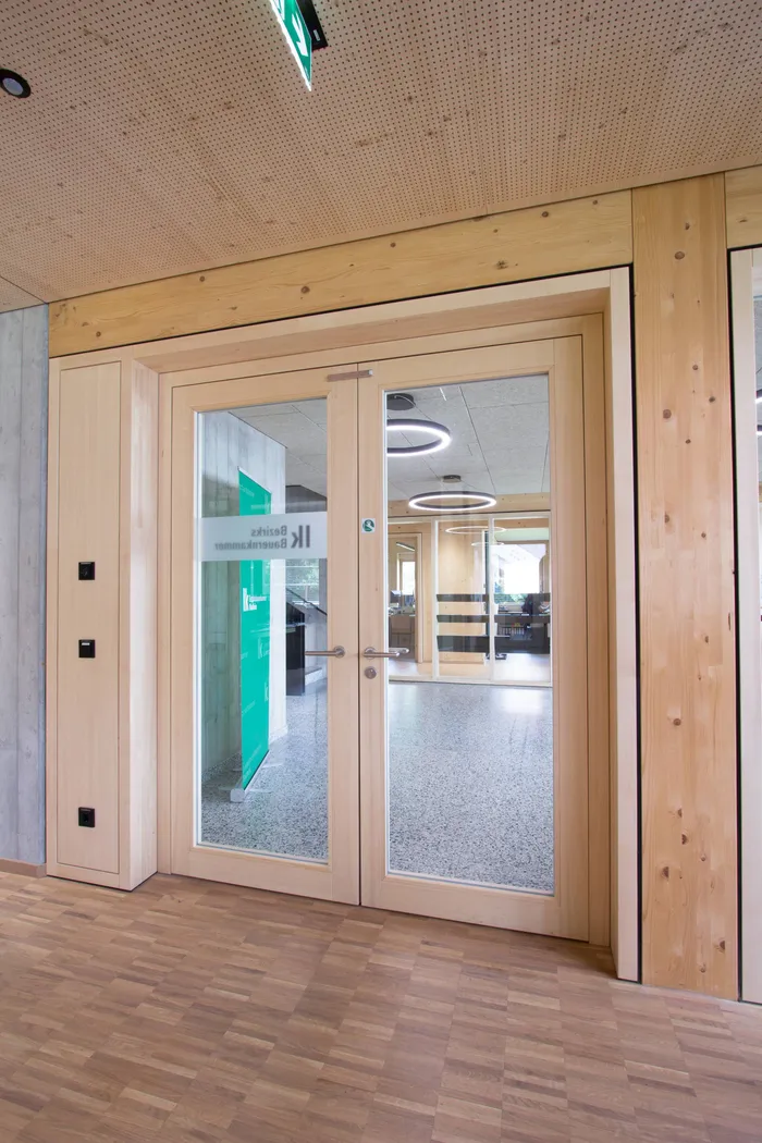 Moderne Glastür mit Holzrahmen in einem Bürogebäude mit Sicht auf den Empfangsbereich