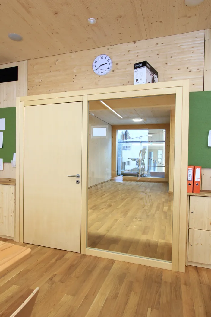 Moderne Holztür mit Glaseinsatz in einem hellen Büroraum mit Parkettboden