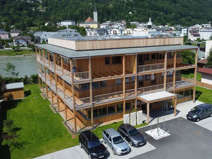 Modernes Holzgebäude mit Balkonen und begrüntem Außenbereich am Flussufer in städtischer Umgebung