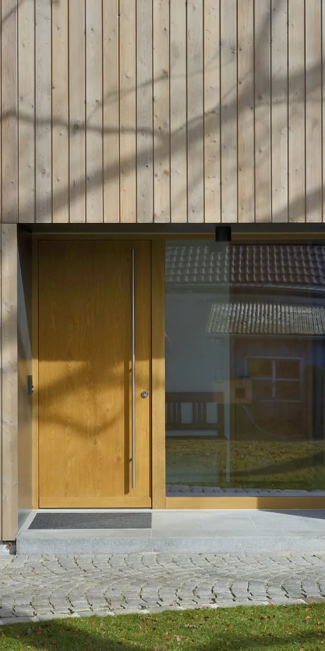 Moderne Holzfassade mit großer Eingangstür und Glasfront in Wohnsiedlung