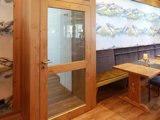 Moderne Holzkabine mit Glastür in einem stilvollen Restaurant mit Wandkunst und Sitzbank