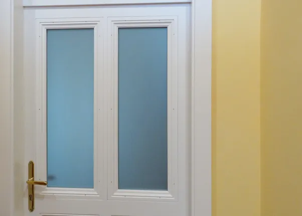 Weiße Tür mit Milchglasfenstern, daneben ein Feuerlöscher und Brandschutzschild an gelber Wand