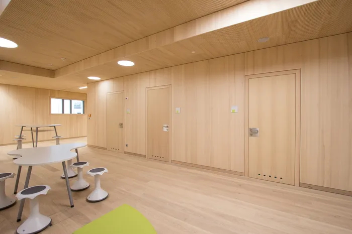 Moderner Klassenraum mit Holzwänden, weißen Tischen und ergonomischen Hockern