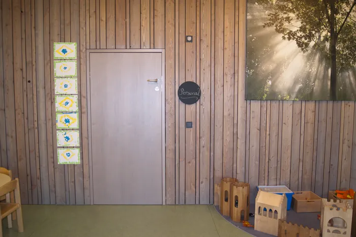 Holzwand mit Tür, Kindergemälden, Spielsachen und einem Bild mit Sonnenstrahlen im Wald