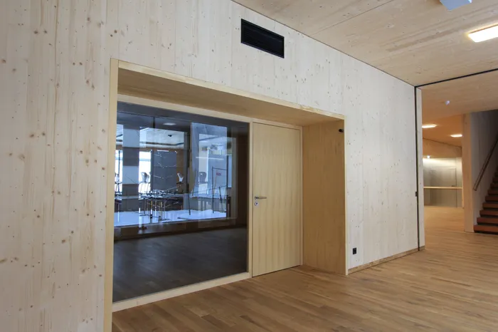 Moderner Innenraum mit hellem Holz, Glastür und Blick in einen leeren Klassenraum