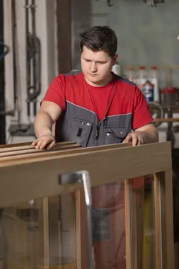 Tischler in Arbeitskleidung prüft Holzrahmen in einer Werkstatt