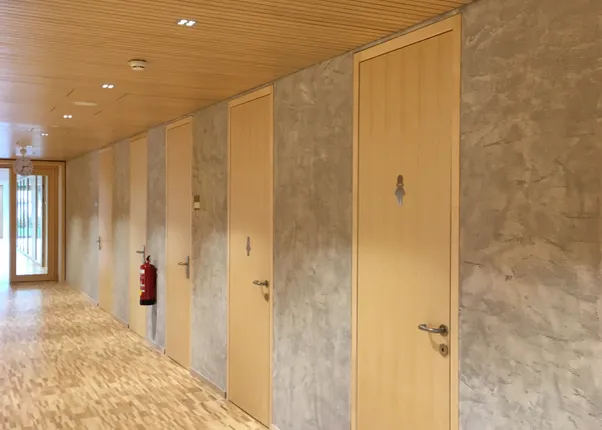 Korridor mit mehreren Holztüren, Parkettboden und moderner Holzdecke in einem öffentlichen Gebäude