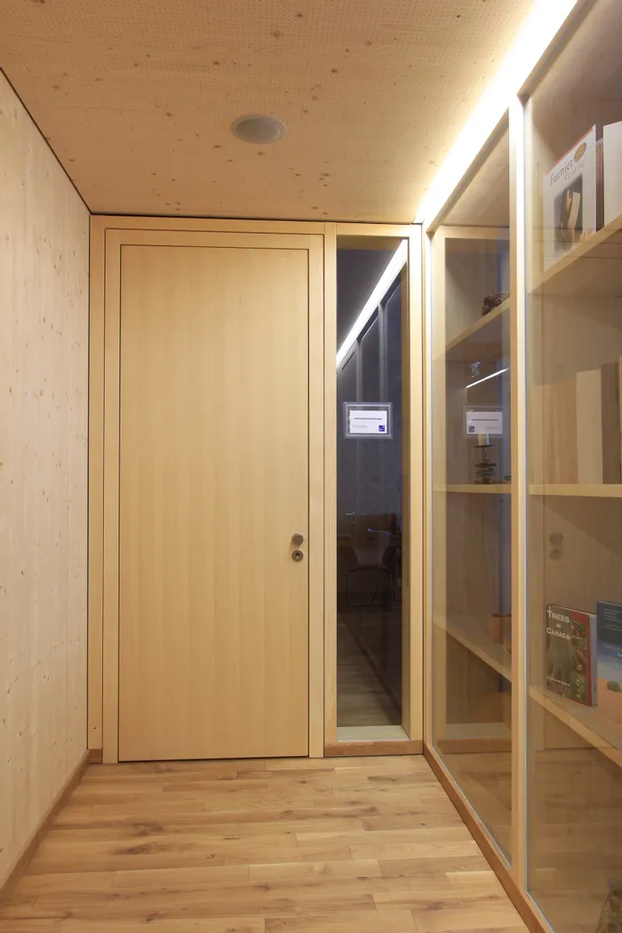 Schmaler Flur mit Holztür, Glaswand und Regalen voller Bücher und Holzproben
