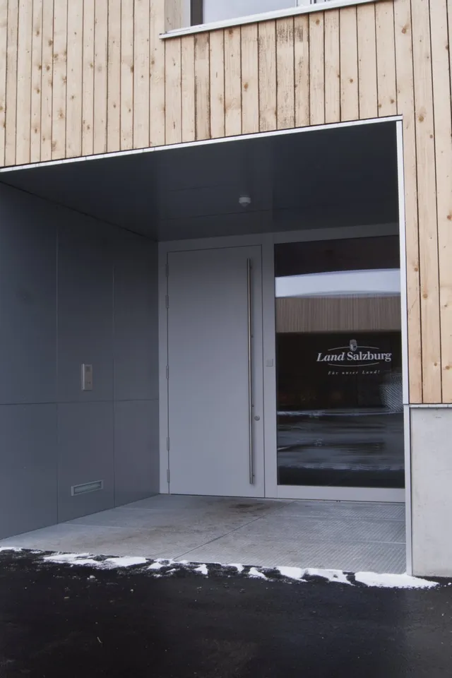 Eingang eines modernen Gebäudes mit Holzwand und Tür mit Aufschrift Land Salzburg