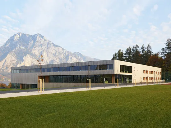 Modernes Schulgebäude mit Holzfassade vor Bergpanorama und grüner Wiese