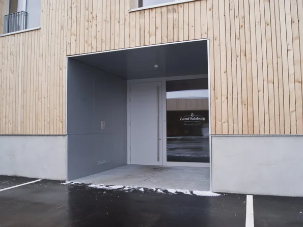 Eingang eines modernen Gebäudes mit Holzfassade und Glastür, Beschriftung Land Salzburg