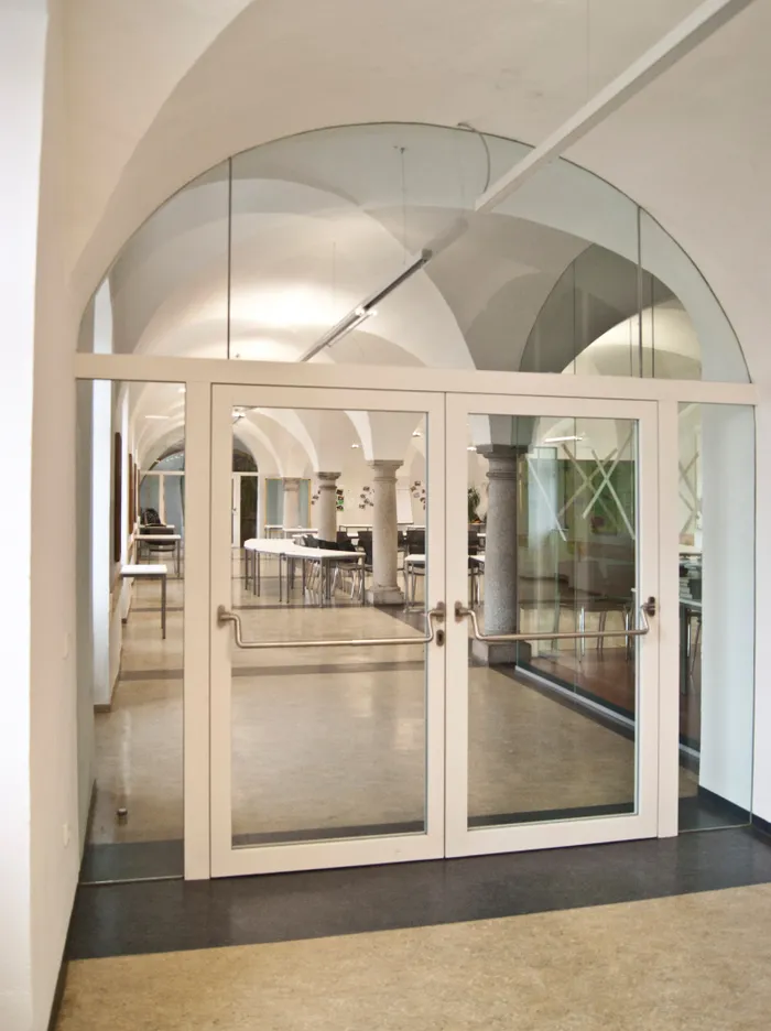 Moderne Glastür mit Blick auf einen hellen Konferenzraum mit Gewölbedecke und Säulen