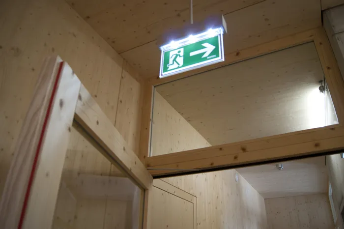 Grünes Notausgangsschild mit Pfeil nach rechts in einem Flur mit Holzverkleidung