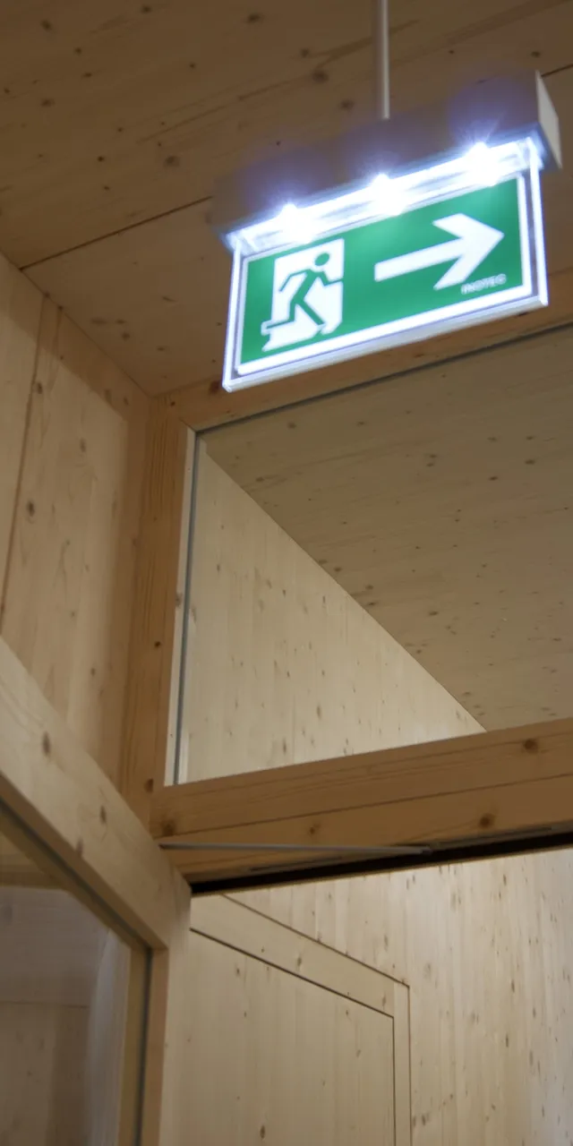 Grünes Notausgangsschild mit Pfeil nach rechts in einem Flur mit Holzverkleidung