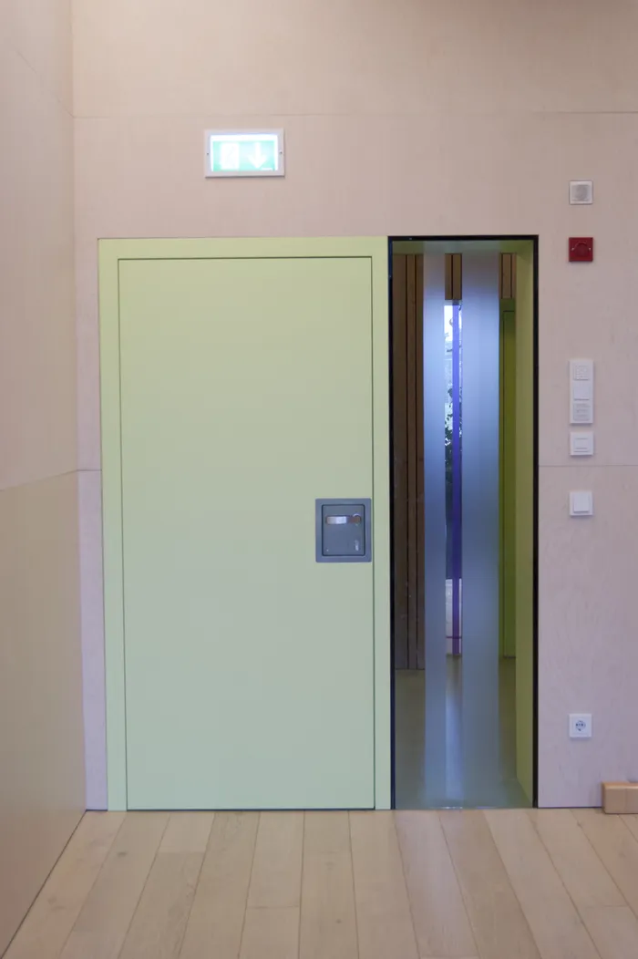 Geöffnete grüne Tür mit Notausgangsschild über einem modernen Innenraum