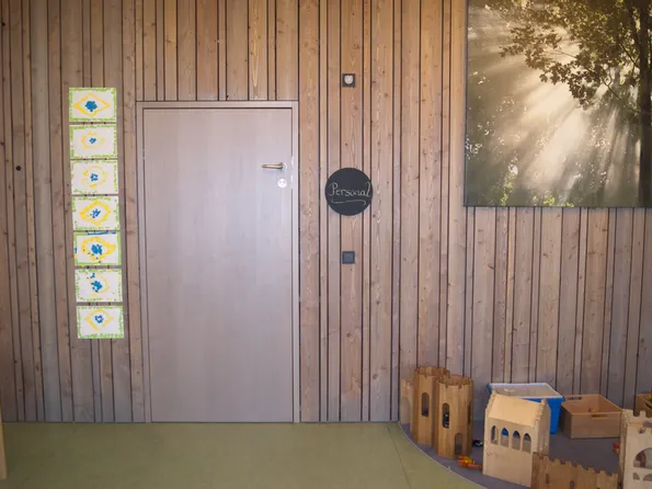 Holzwand mit Tür, Kindergemälden, Spielsachen und einem Bild mit Sonnenstrahlen im Wald