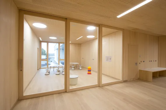 Moderner Kindergartenraum mit Holzwänden, kleinen Tischen und buntem Spielzeug