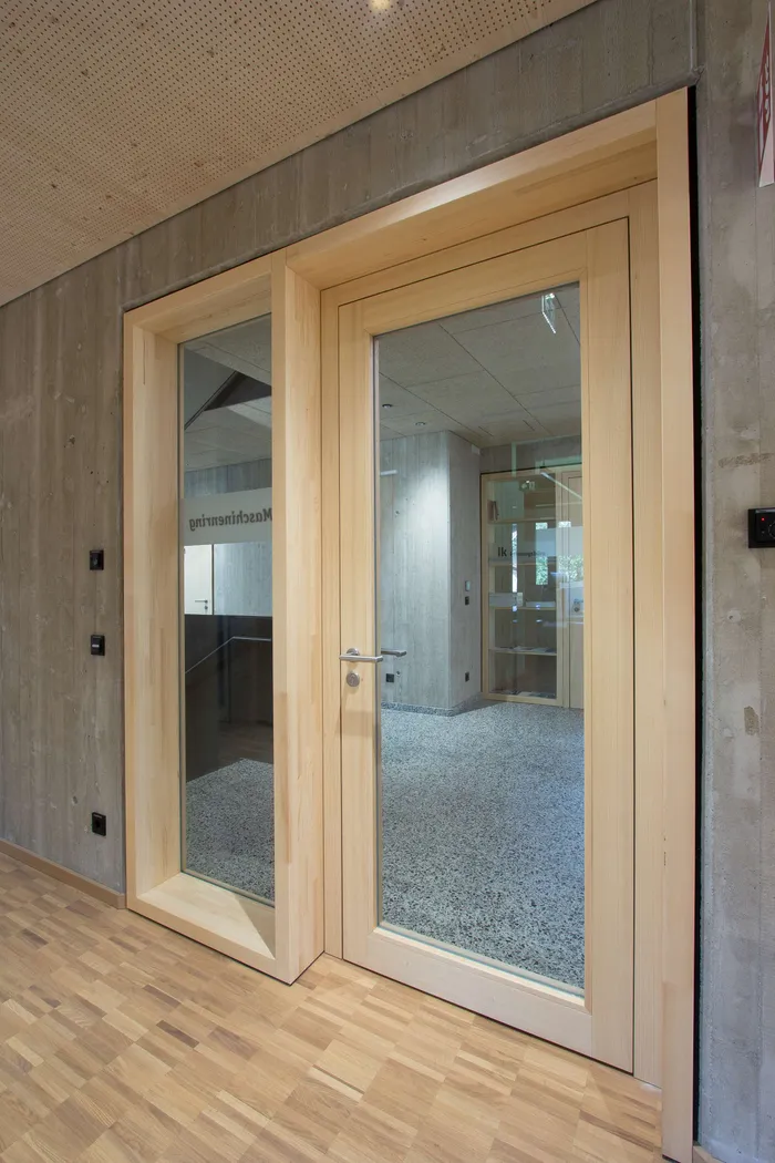 Moderne Innentür aus hellem Holz mit Glasfenster in Betonwand eingebaut