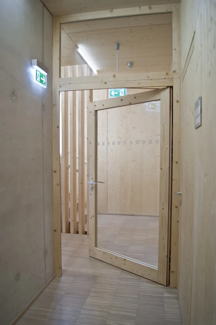 Offene Glastür in modernem Innenraum mit Holzwänden und Notausgangsschildern