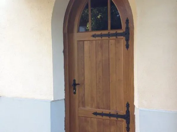 Holztür mit Spitzbogen und schmiedeeisernen Beschlägen an einem verputzten Gebäude