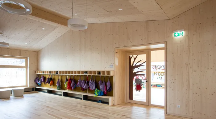 Heller Garderobenraum in einer Kita mit Holzwänden und bunten Kindertaschen an Haken