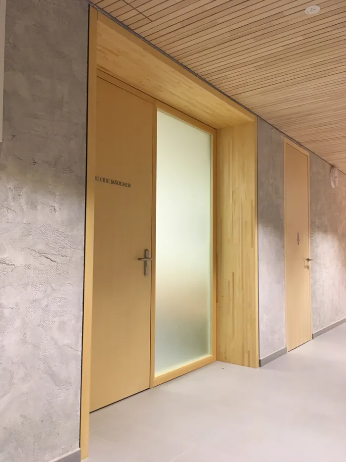 Holztür mit der Aufschrift 'KLEIDE MÄDCHEN' in einem modernen Innenflur