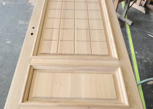 Massive unbehandelte Holzhaustür mit quadratischem Kassettenmuster in Werkstattumgebung