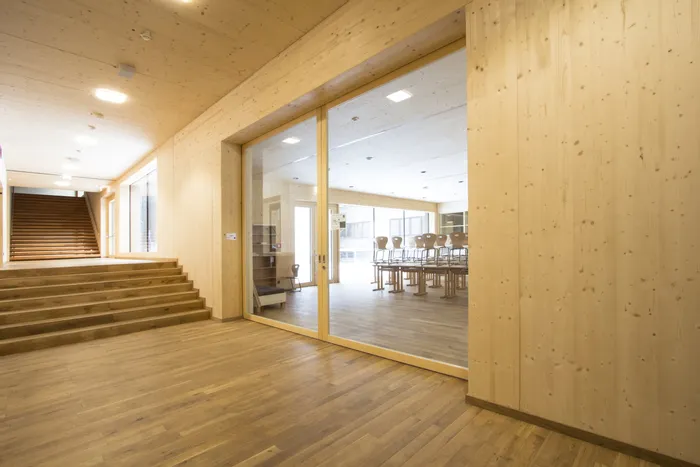Moderner Schulflur mit Holzverkleidung und Blick in ein leeres Klassenzimmer mit gestapelten Stühlen