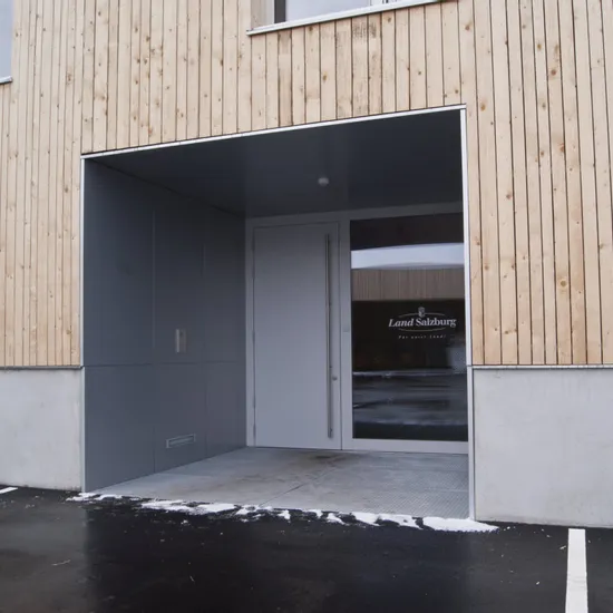 Eingang eines modernen Gebäudes mit Holzwand und Tür mit Aufschrift Land Salzburg