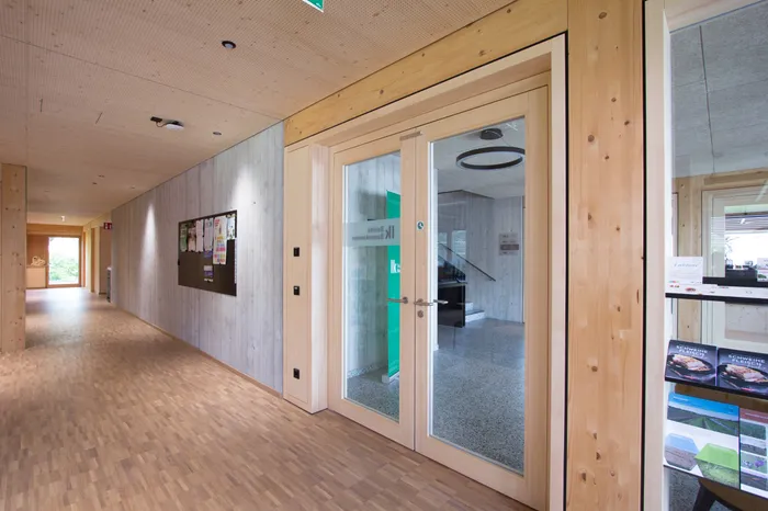 Moderner Büroflur mit Holzboden, Glastür und Pinnwand an der Wand