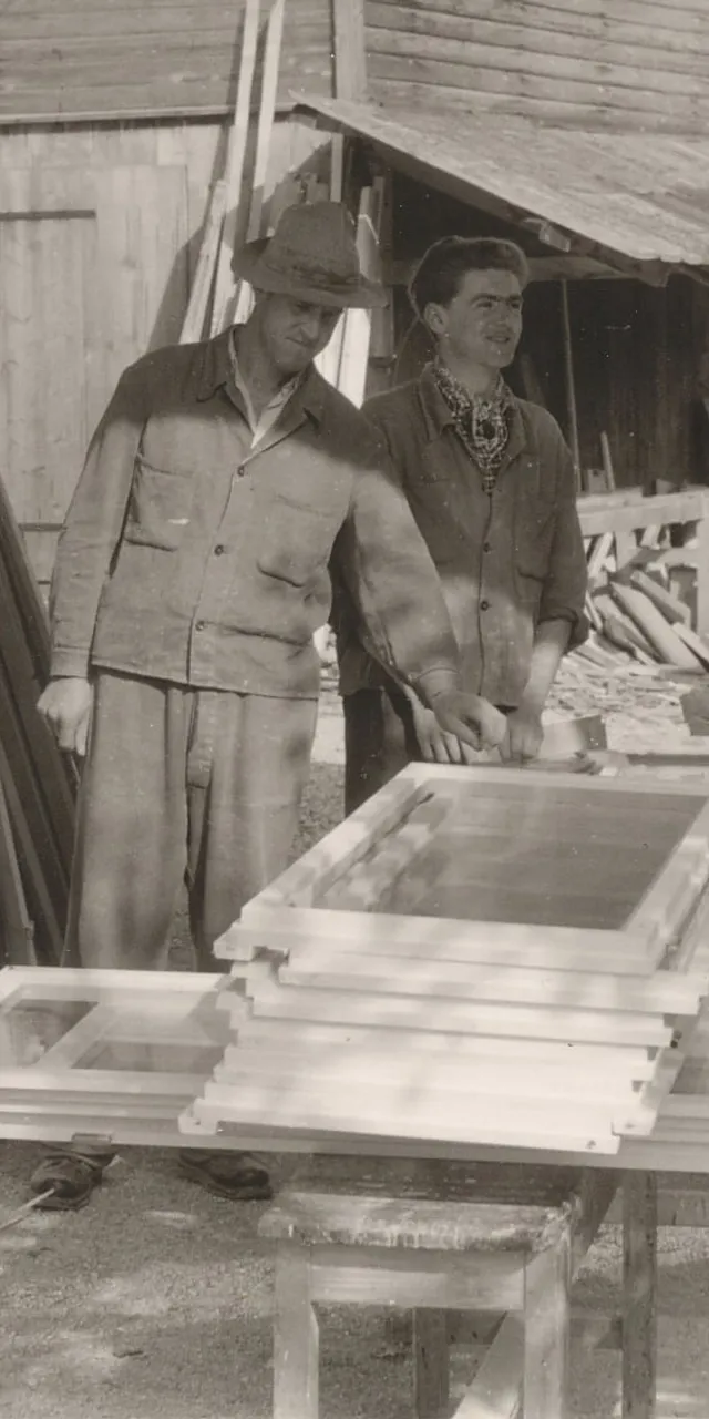 Vier Schreiner arbeiten im Freien an Holzrahmen vor einer Werkstatt