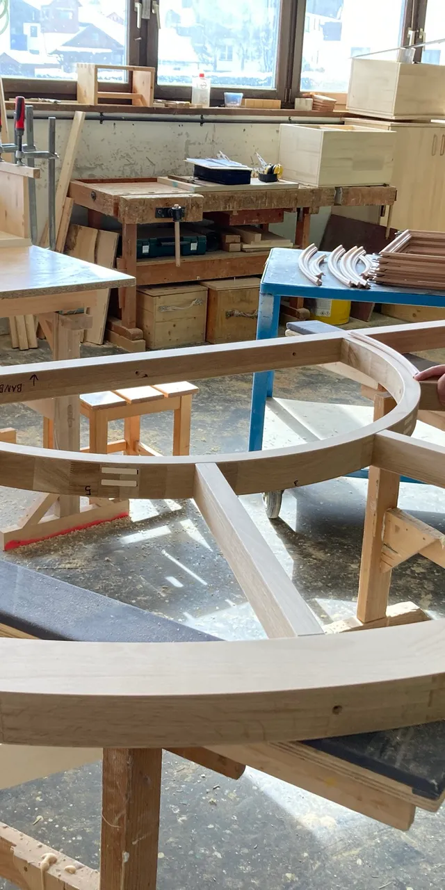 Tischler arbeitet an einem großen runden Holzrahmen in einer gut ausgestatteten Werkstatt