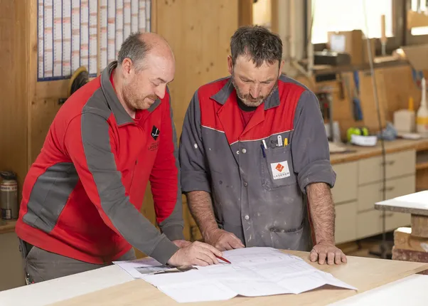 Zwei Handwerker prüfen Bauzeichnungen in einer Holzwerkstatt