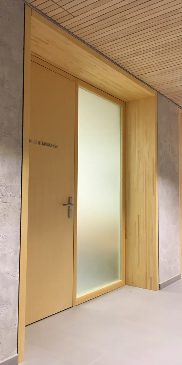Holztür mit der Aufschrift 'KLEIDE MÄDCHEN' in einem modernen Innenflur