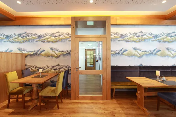 Gemütlicher Restaurantbereich mit Holzmöbeln und Wandbild in Berglandschaft-Optik