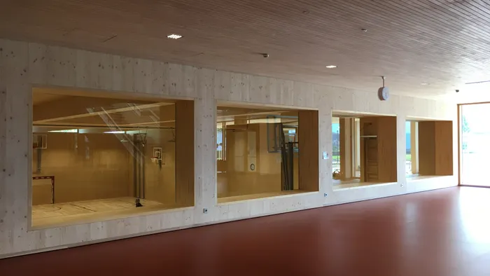 Große Fenster mit Blick in eine moderne Sporthalle mit Holzwänden und Basketballkörben