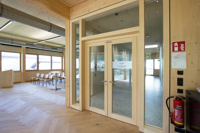 Moderner Innenraum aus Holz mit Glastür zum Saal Halion und Stuhlreihe neben großen Fenstern