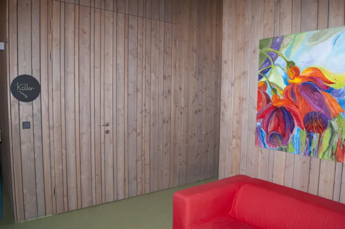 Holzverkleidete Wand mit getarnter Kellertür, rotem Sofa und buntem Blumenbild