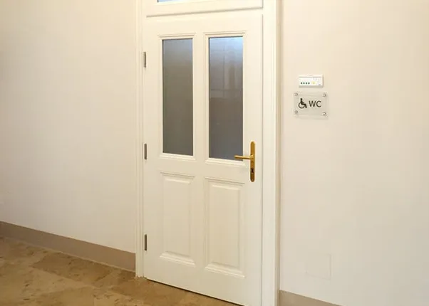 Weiße WC-Tür mit Glaseinsätzen und Schild für barrierefreie Toilette an der Wand