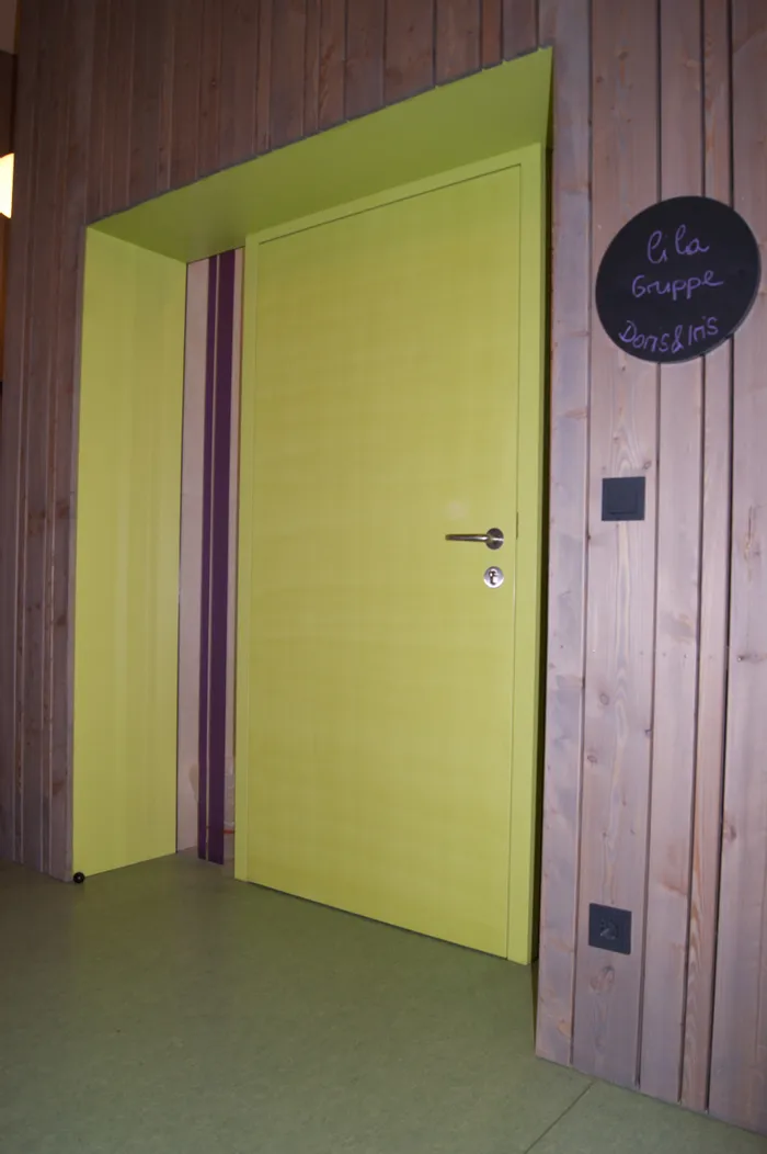 Gelbe Tür in Holzverkleidung mit Schild zur lila Gruppe von Doris und Iris